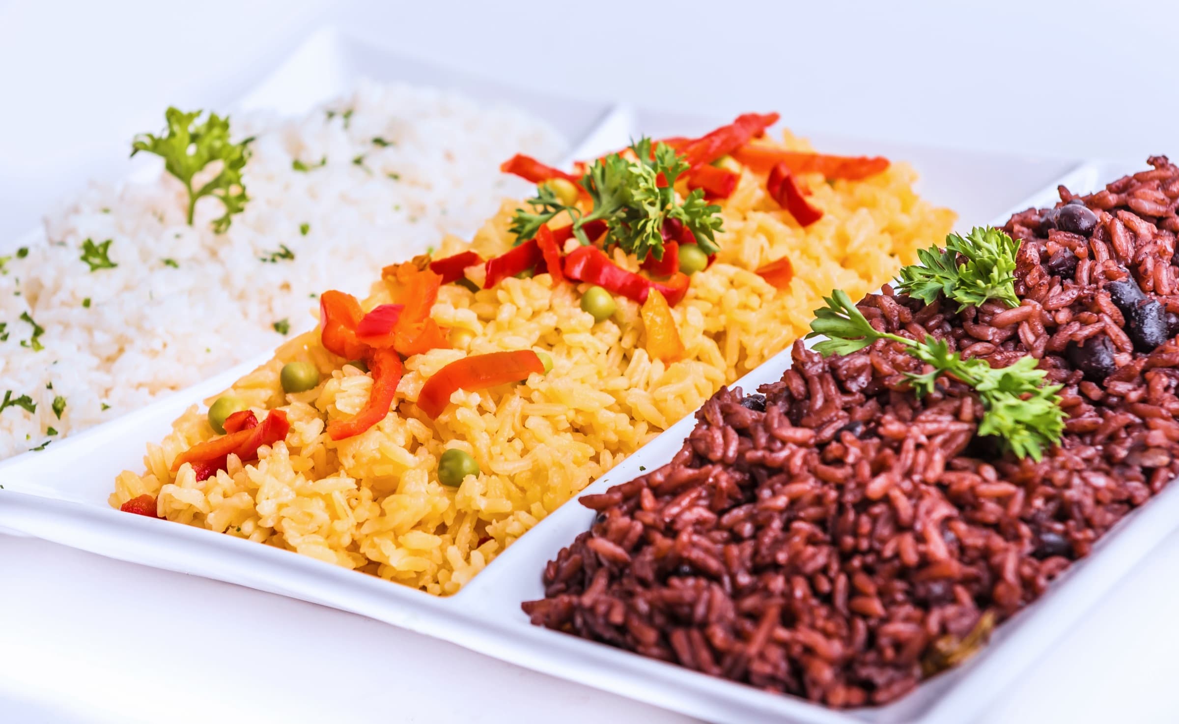 White rice, yellow rice with peppers and peas, and congrí served side by side on a white platter
