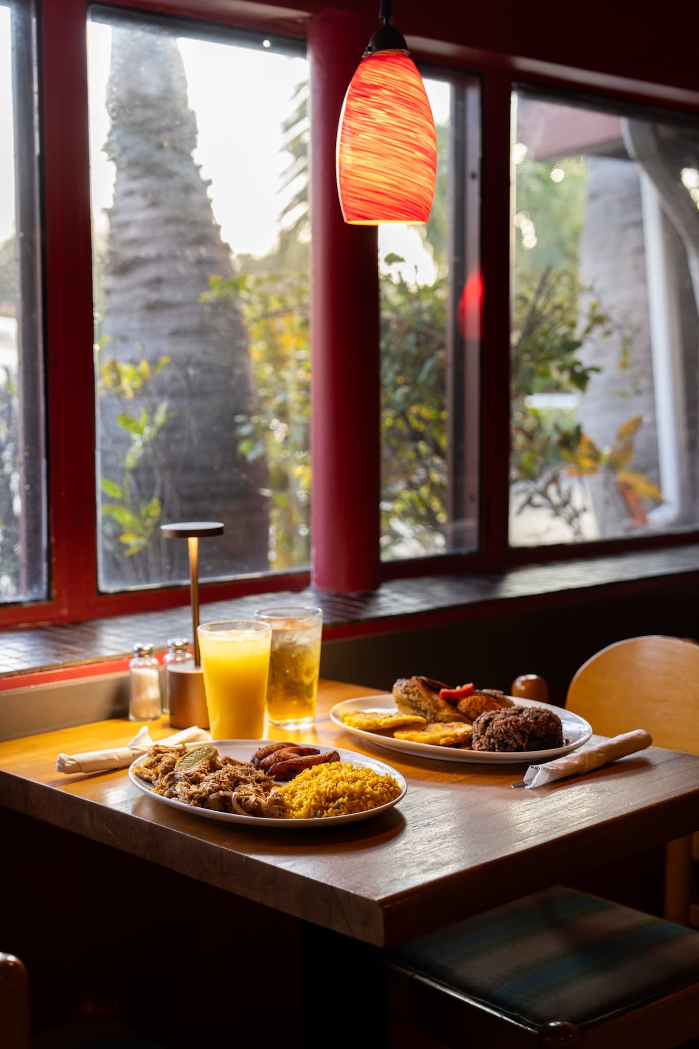 Two Cuban plates in a window booth under a red pendant lamp
