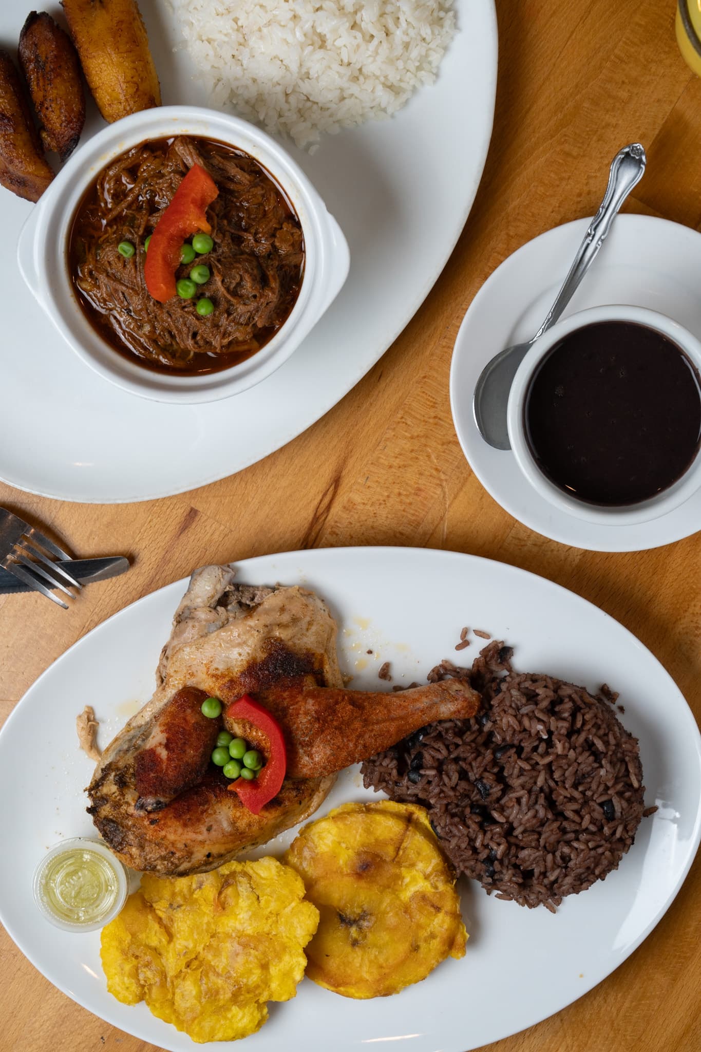 Two plates on one table — roast chicken with congrí and tostones, and a cazuela of beef stew with rice