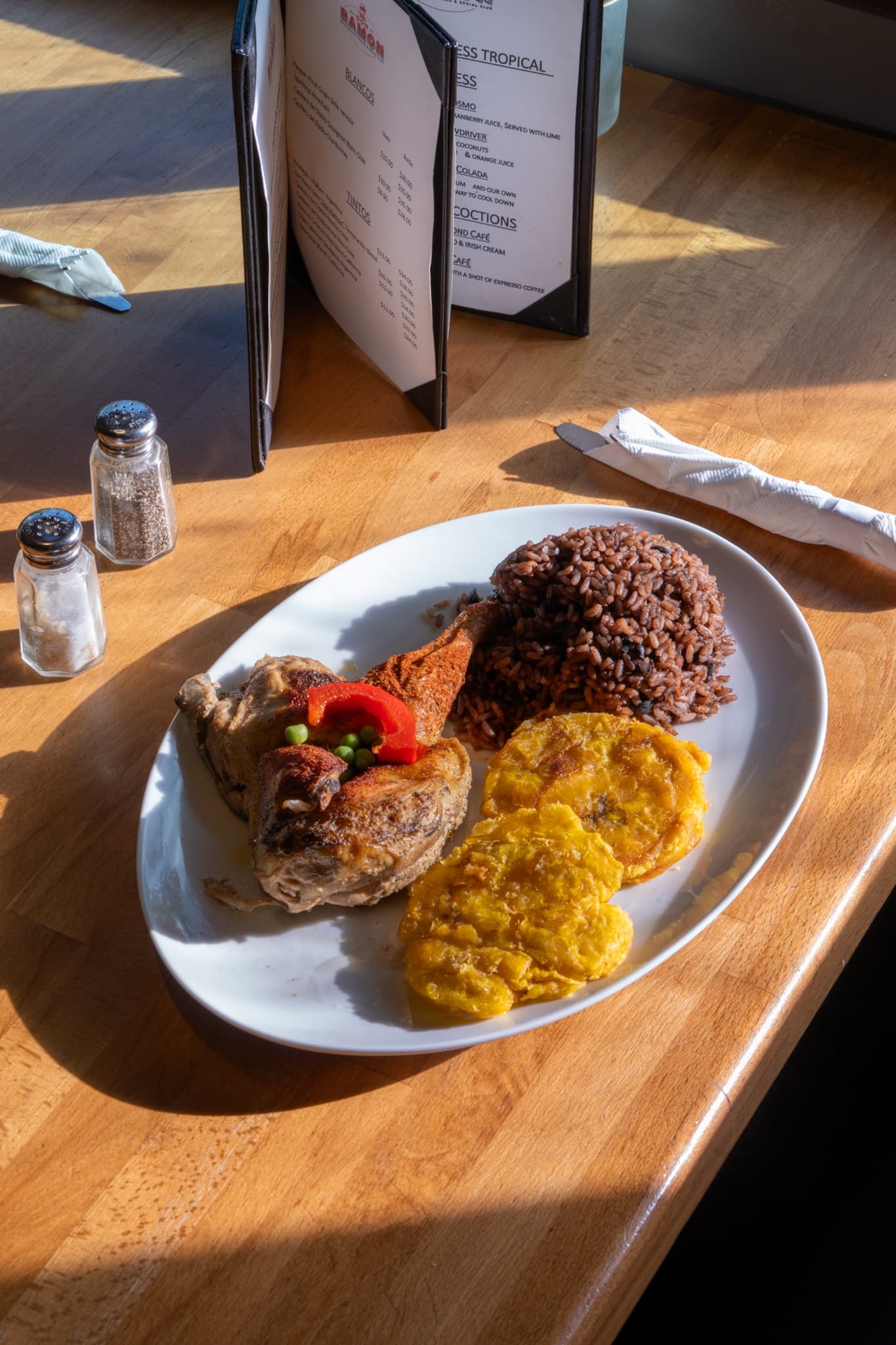 Roast chicken with red beans and tostones in the sunlight of a window table