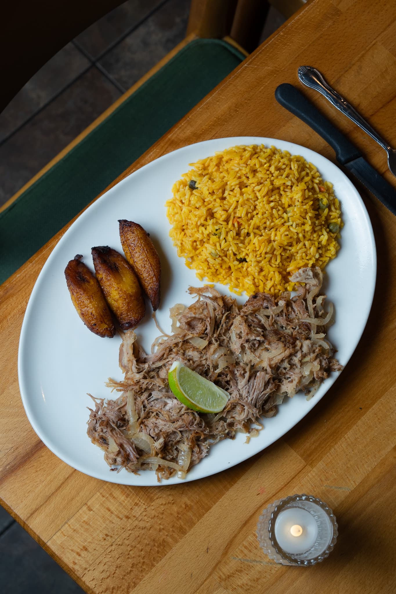Lechón asado, yellow rice and sweet plantains on a wooden table by candlelight