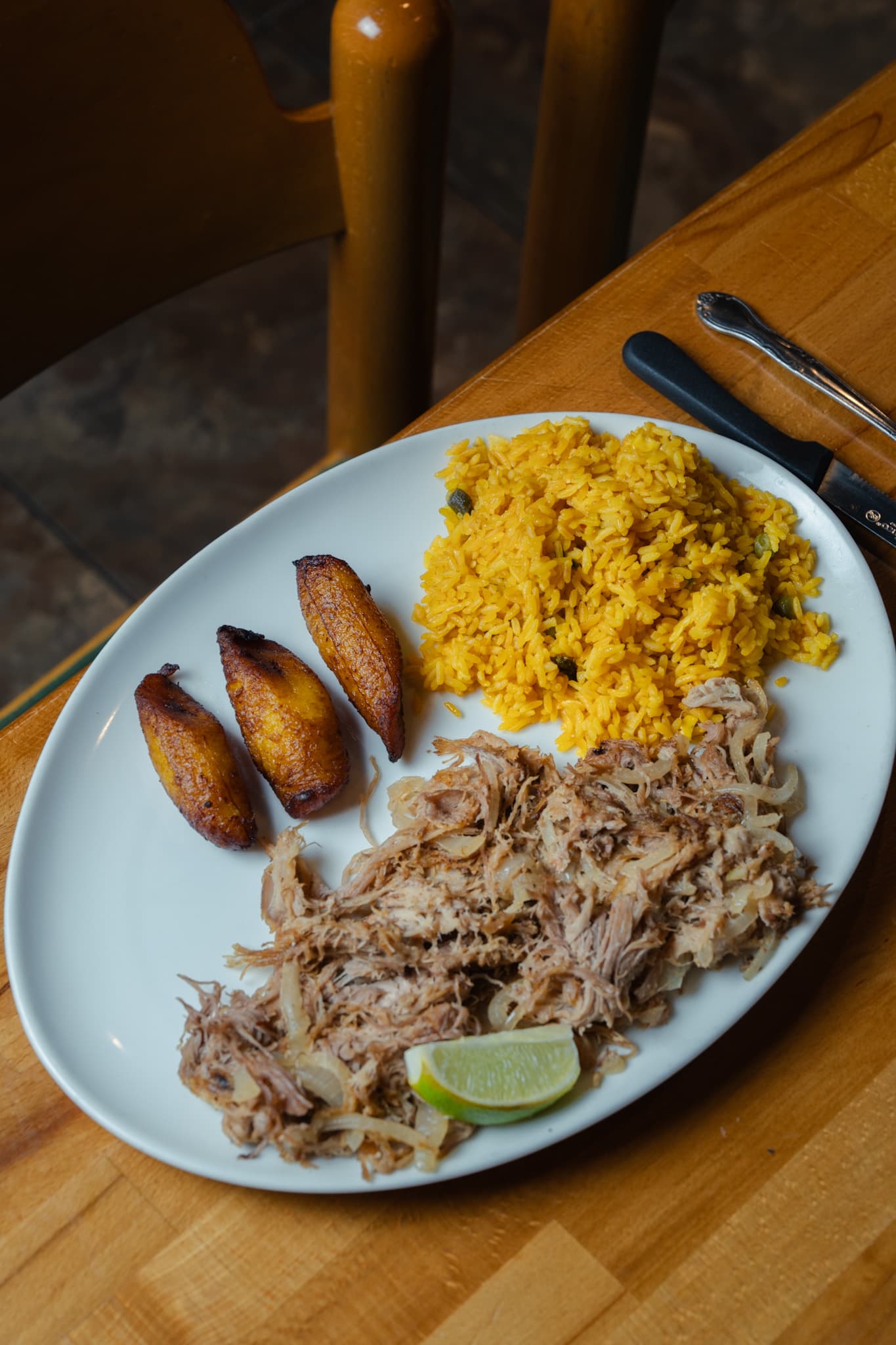 Shredded lechón asado with yellow rice, sweet plantains and a wedge of lime