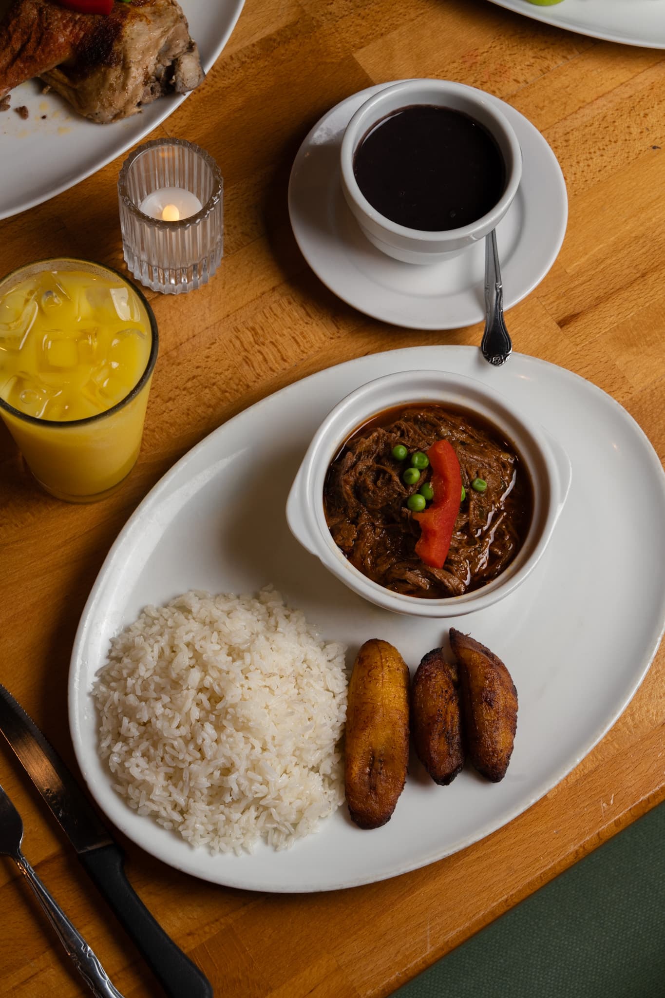 A cazuela of beef stew with white rice, sweet plantains, black bean soup and fresh juice