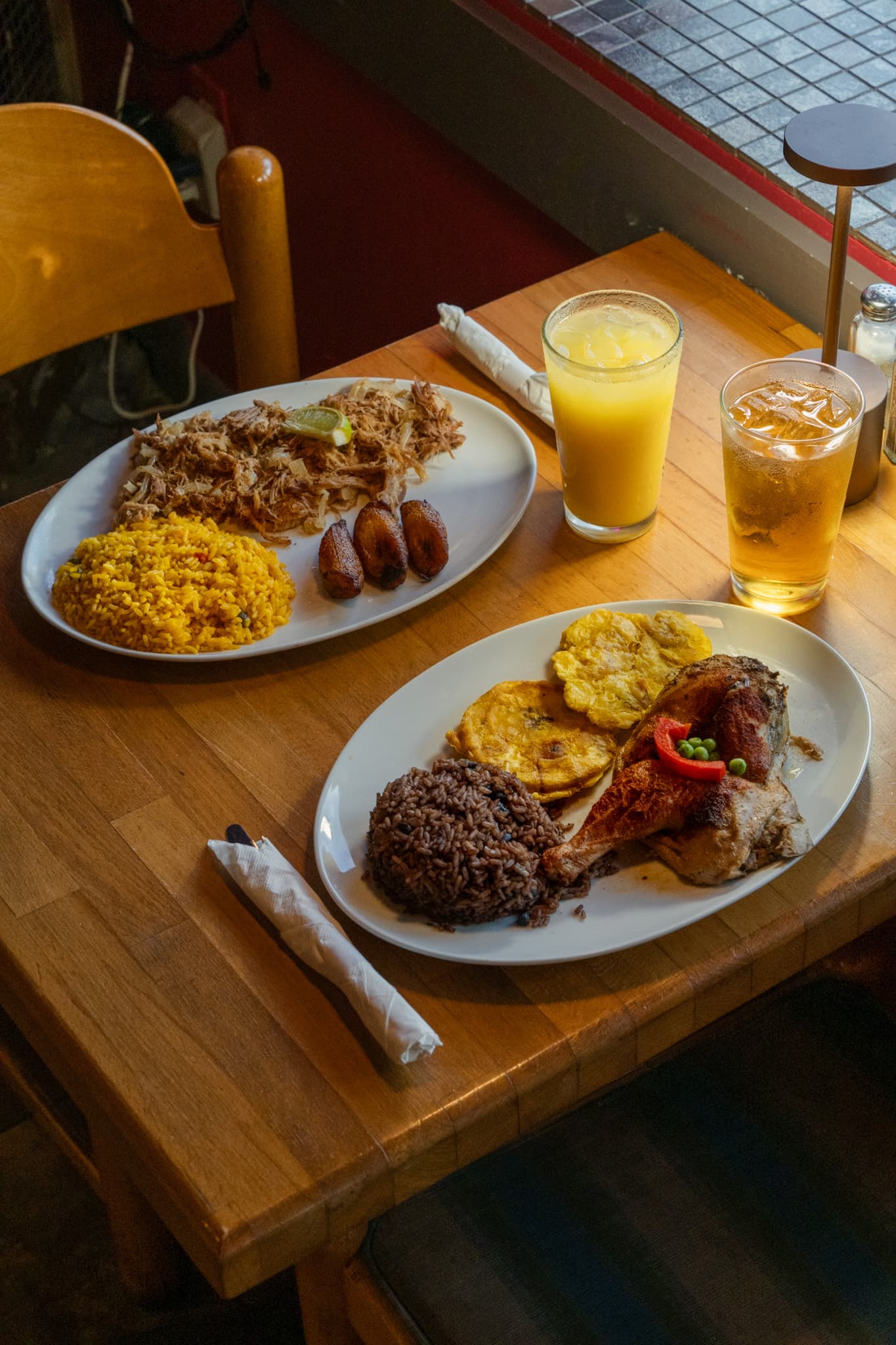 Two plates of Cuban food with yellow rice, black beans and tostones on a wooden table
